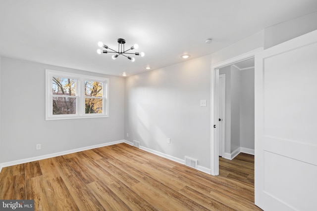 empty room with a notable chandelier and wood-type flooring