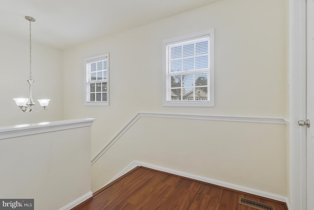 empty room with hardwood / wood-style flooring and an inviting chandelier