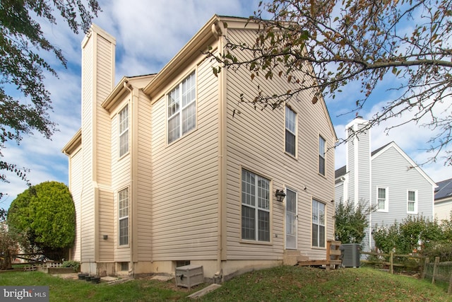 rear view of house featuring central AC unit and a lawn