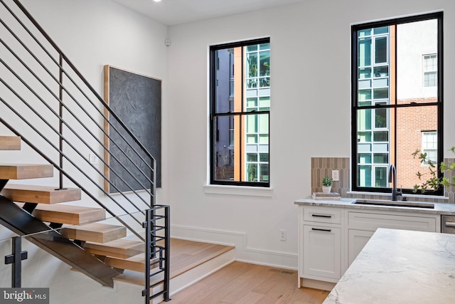 interior space with light hardwood / wood-style floors, light stone countertops, white cabinetry, and sink