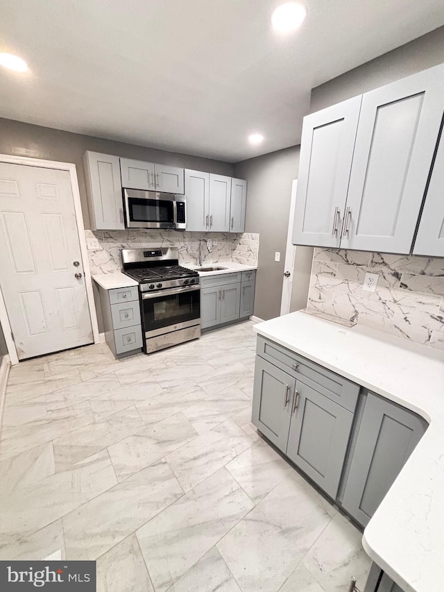 kitchen with decorative backsplash, stainless steel appliances, gray cabinetry, and sink