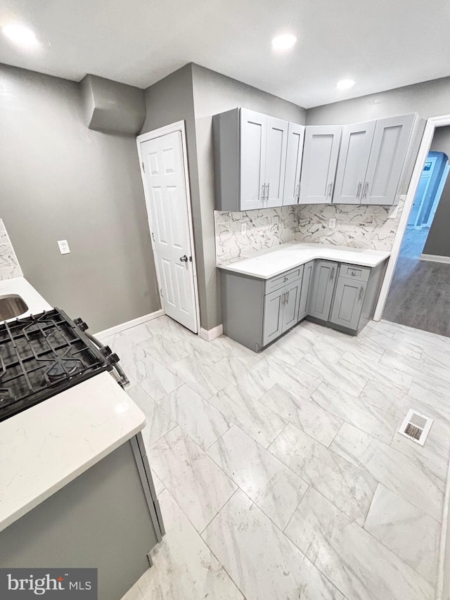 kitchen featuring tasteful backsplash, gray cabinetry, and light stone counters