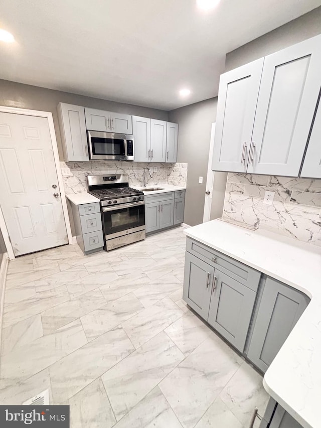 kitchen with appliances with stainless steel finishes, backsplash, and gray cabinetry