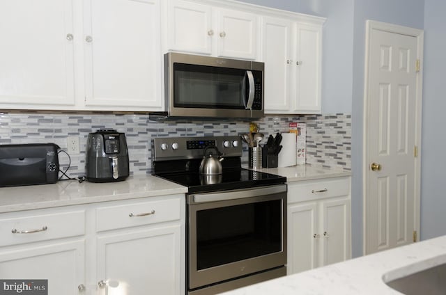 kitchen with light stone countertops, decorative backsplash, stainless steel appliances, and white cabinetry