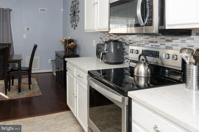 kitchen with white cabinets, stainless steel appliances, tasteful backsplash, and light hardwood / wood-style floors