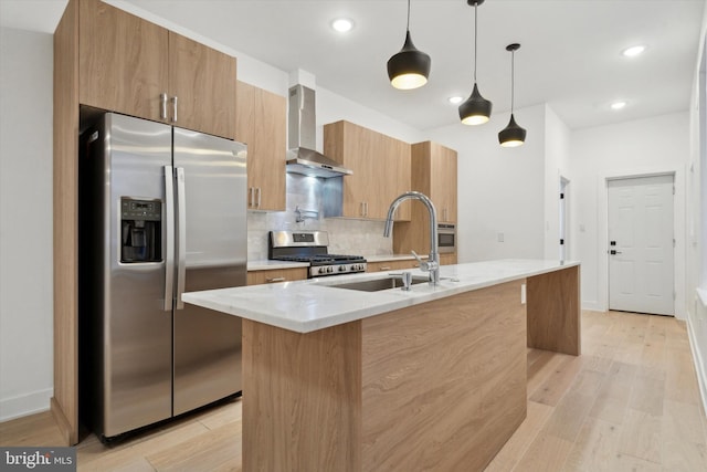 kitchen with sink, wall chimney exhaust hood, stainless steel appliances, pendant lighting, and a center island with sink