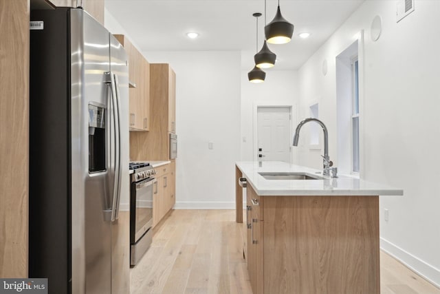 kitchen with sink, light hardwood / wood-style floors, pendant lighting, a center island with sink, and appliances with stainless steel finishes