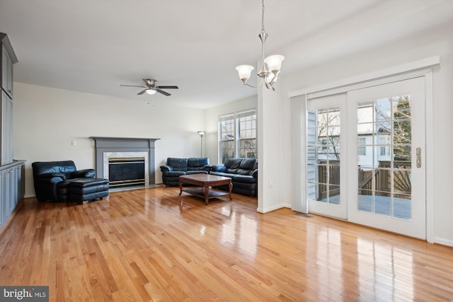 living room featuring ceiling fan with notable chandelier, light hardwood / wood-style flooring, and a premium fireplace