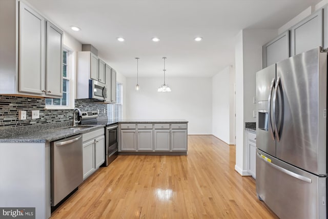 kitchen featuring gray cabinetry, hanging light fixtures, stainless steel appliances, light hardwood / wood-style flooring, and kitchen peninsula