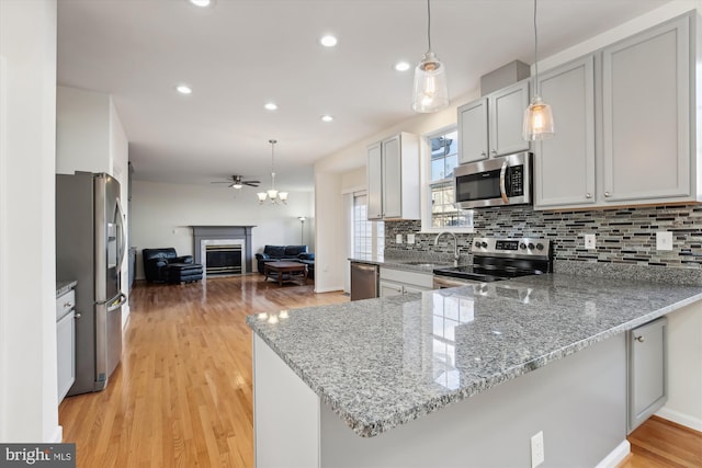 kitchen with kitchen peninsula, pendant lighting, light wood-type flooring, and appliances with stainless steel finishes