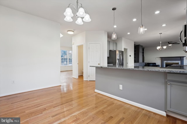 kitchen featuring gray cabinetry, dark stone counters, ceiling fan with notable chandelier, light hardwood / wood-style floors, and stainless steel fridge with ice dispenser