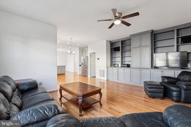 living room with ceiling fan with notable chandelier and light wood-type flooring