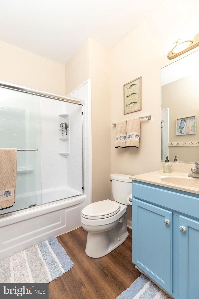 full bathroom with hardwood / wood-style floors, combined bath / shower with glass door, toilet, and vanity