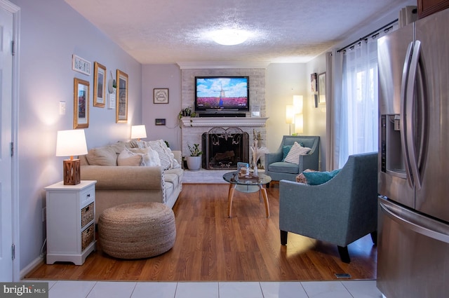 living room featuring hardwood / wood-style flooring, a textured ceiling, and a brick fireplace