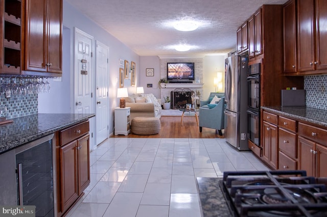 kitchen featuring beverage cooler, dark stone counters, a textured ceiling, decorative backsplash, and black appliances