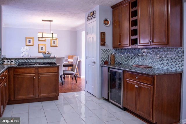 kitchen with dark stone counters, crown molding, pendant lighting, and beverage cooler