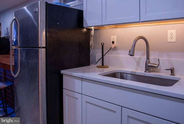 kitchen with white cabinets, light stone counters, sink, and stainless steel refrigerator