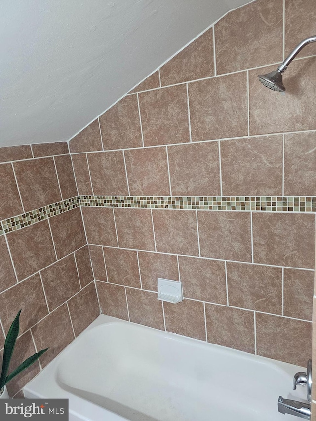 bathroom featuring vaulted ceiling and tiled shower / bath