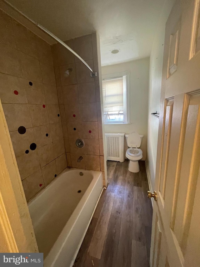 bathroom with radiator heating unit, tiled shower / bath combo, hardwood / wood-style flooring, and toilet