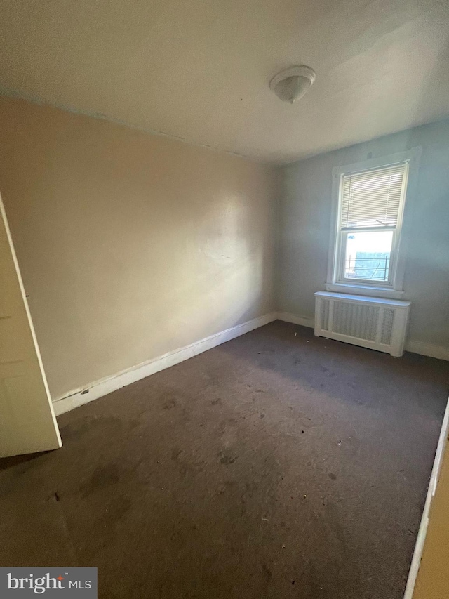 empty room featuring dark colored carpet and radiator