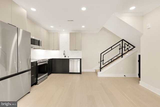 kitchen with appliances with stainless steel finishes, backsplash, ornamental molding, sink, and light hardwood / wood-style flooring