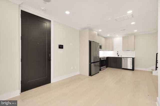 kitchen featuring appliances with stainless steel finishes, backsplash, crown molding, sink, and light hardwood / wood-style floors