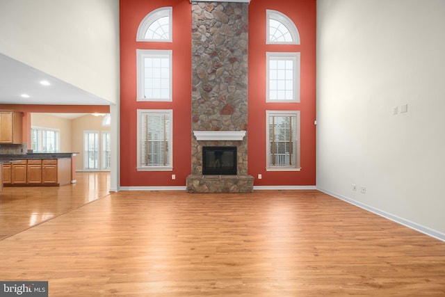 unfurnished living room featuring light wood-type flooring, a towering ceiling, and a fireplace