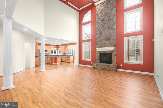 unfurnished living room with decorative columns, a fireplace, a towering ceiling, and light hardwood / wood-style floors