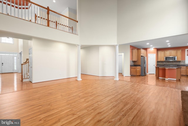 unfurnished living room featuring a high ceiling and light hardwood / wood-style flooring