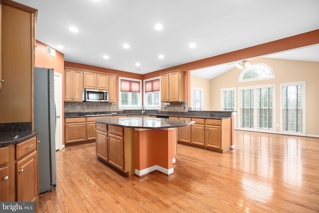 kitchen with stainless steel appliances, tasteful backsplash, light hardwood / wood-style flooring, lofted ceiling, and a kitchen island