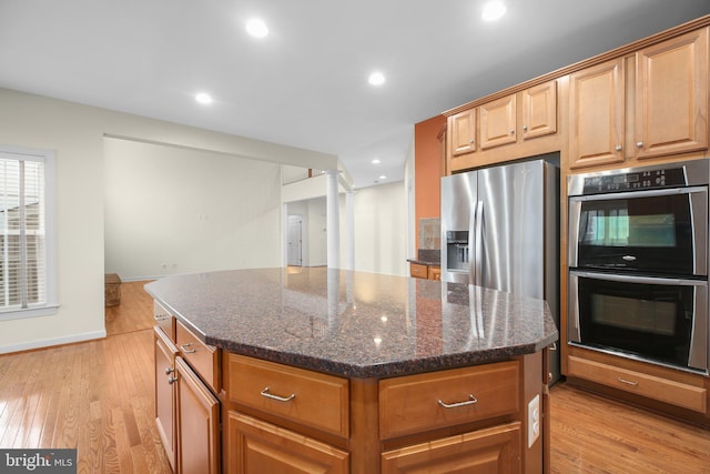 kitchen with ornate columns, dark stone counters, stainless steel appliances, light hardwood / wood-style flooring, and a center island