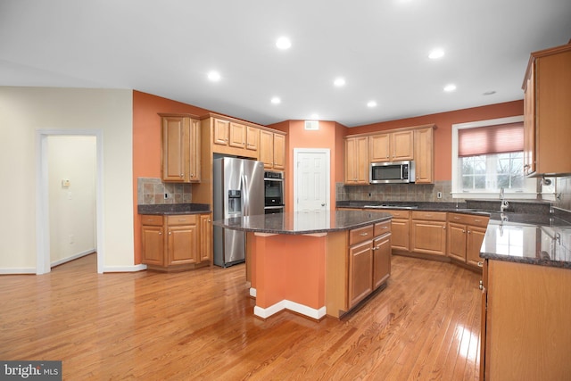 kitchen with light wood-type flooring, tasteful backsplash, stainless steel appliances, dark stone countertops, and a center island