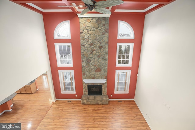 unfurnished living room featuring crown molding, light hardwood / wood-style flooring, ceiling fan, a fireplace, and beam ceiling