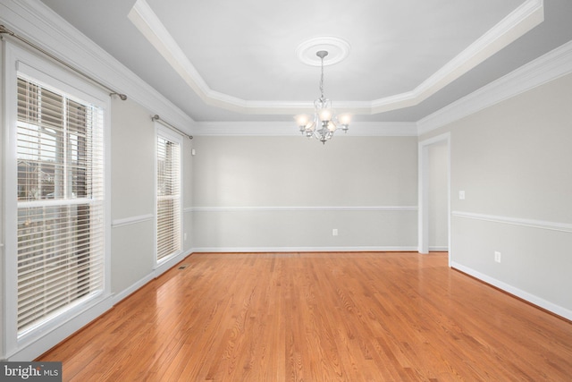 spare room featuring a raised ceiling, an inviting chandelier, ornamental molding, and light wood-type flooring