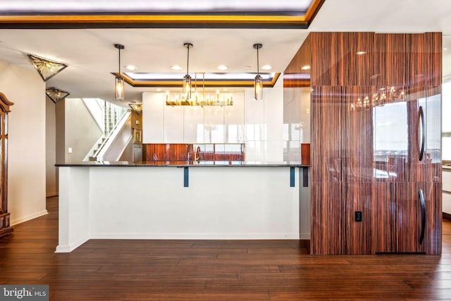 kitchen with kitchen peninsula, dark hardwood / wood-style flooring, a tray ceiling, sink, and hanging light fixtures