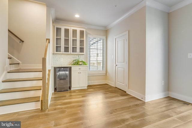 bar featuring decorative backsplash, light hardwood / wood-style flooring, white cabinetry, and ornamental molding