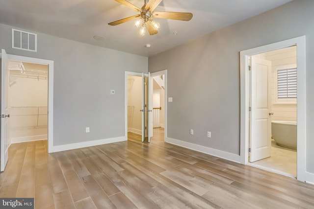 unfurnished bedroom featuring connected bathroom, a spacious closet, ceiling fan, a closet, and light wood-type flooring