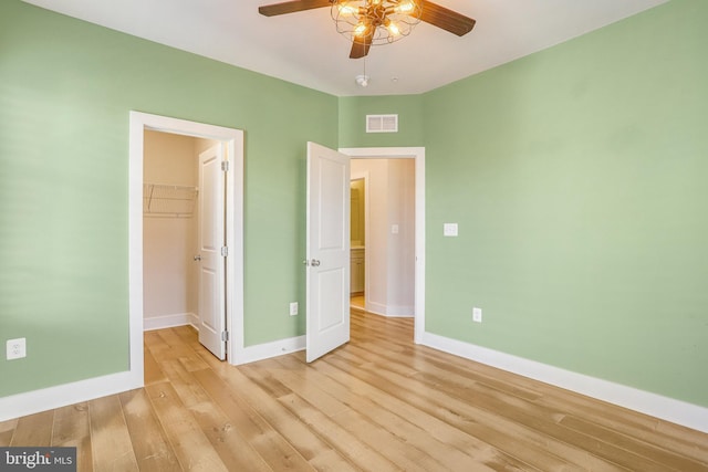 unfurnished bedroom featuring ceiling fan, light hardwood / wood-style floors, a walk in closet, and a closet