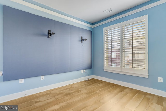 empty room with crown molding and light hardwood / wood-style floors