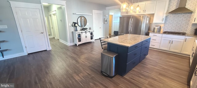 kitchen with pendant lighting, wall chimney exhaust hood, stainless steel fridge, and white cabinets