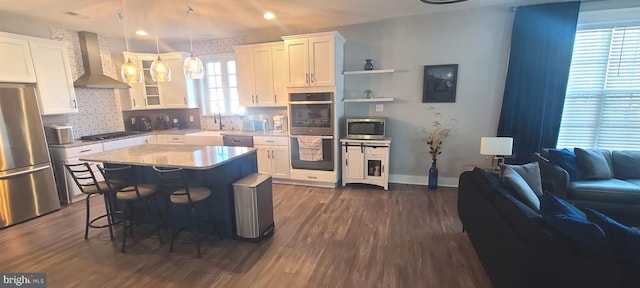 kitchen with pendant lighting, wall chimney range hood, dark hardwood / wood-style floors, white cabinetry, and stainless steel appliances