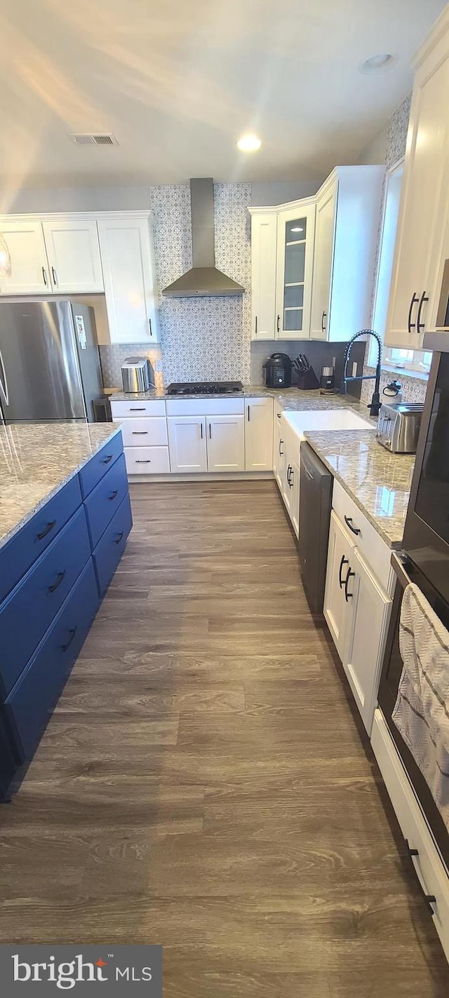 kitchen with white cabinetry, stainless steel fridge, and wall chimney range hood