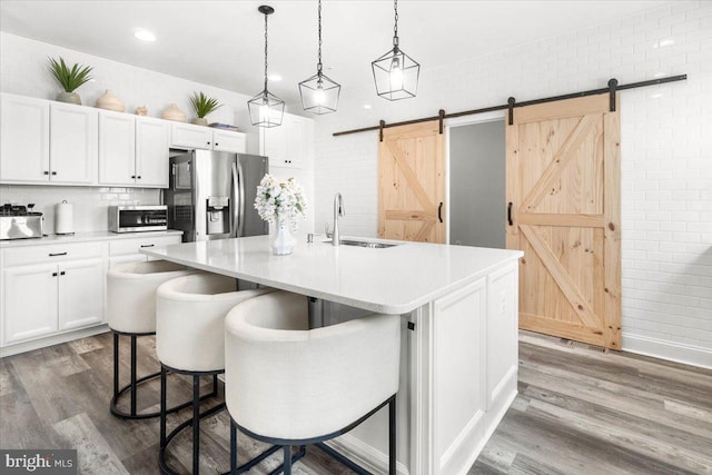 kitchen featuring sink, white cabinetry, a barn door, a kitchen island with sink, and stainless steel appliances