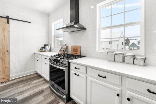 kitchen featuring hardwood / wood-style flooring, white cabinets, a barn door, stainless steel gas range oven, and wall chimney range hood