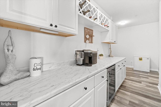 kitchen featuring white cabinets, light wood-type flooring, light stone countertops, and beverage cooler