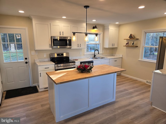 kitchen with wood counters, appliances with stainless steel finishes, sink, decorative light fixtures, and white cabinetry