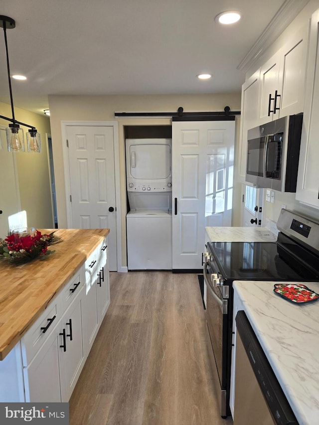 kitchen with stacked washing maching and dryer, stainless steel appliances, a barn door, butcher block countertops, and white cabinetry