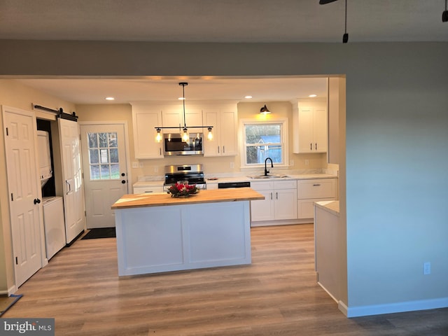 kitchen featuring white cabinetry, hanging light fixtures, a barn door, stacked washer and dryer, and appliances with stainless steel finishes