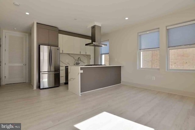 kitchen featuring appliances with stainless steel finishes, backsplash, island range hood, white cabinets, and light hardwood / wood-style floors