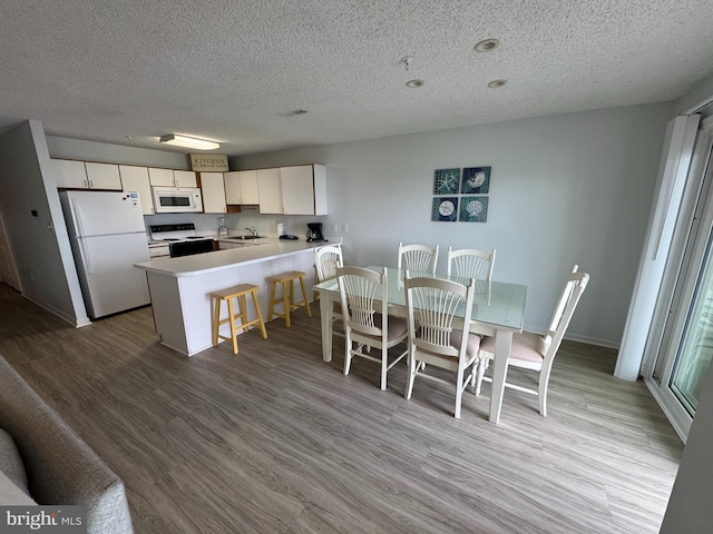 kitchen featuring kitchen peninsula, a textured ceiling, white appliances, and light hardwood / wood-style flooring